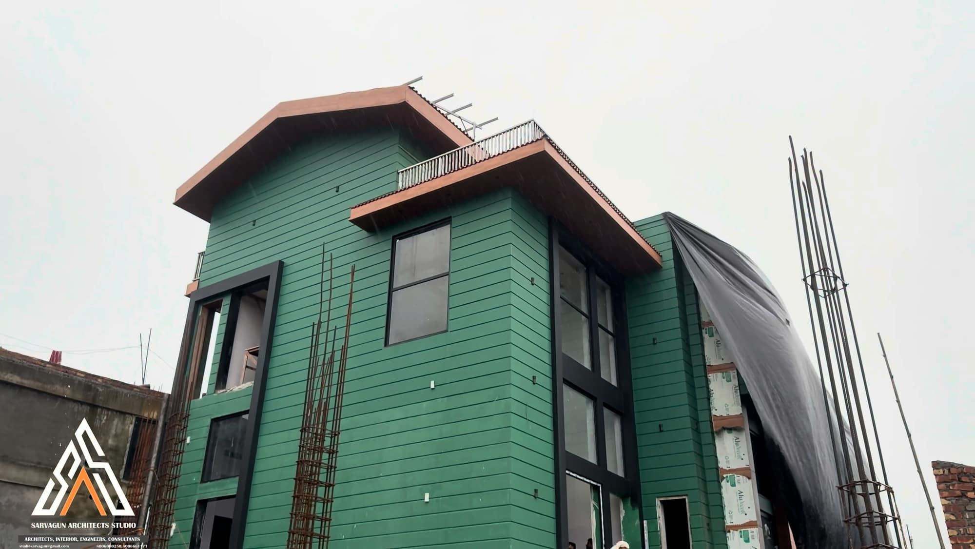 A house mid-construction, wrapped in weatherproofing with exposed rebar